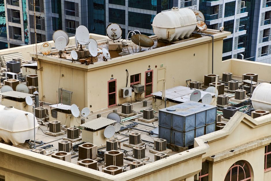 Low-slope urban rooftop seen from above, with vents, tanks and rooftop units.